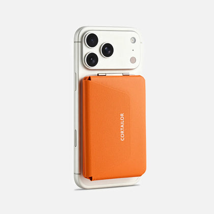 Orange MagSafe leather wallet stand attached to a white iPhone, showing the closed front cover and CORTAILOR logo.